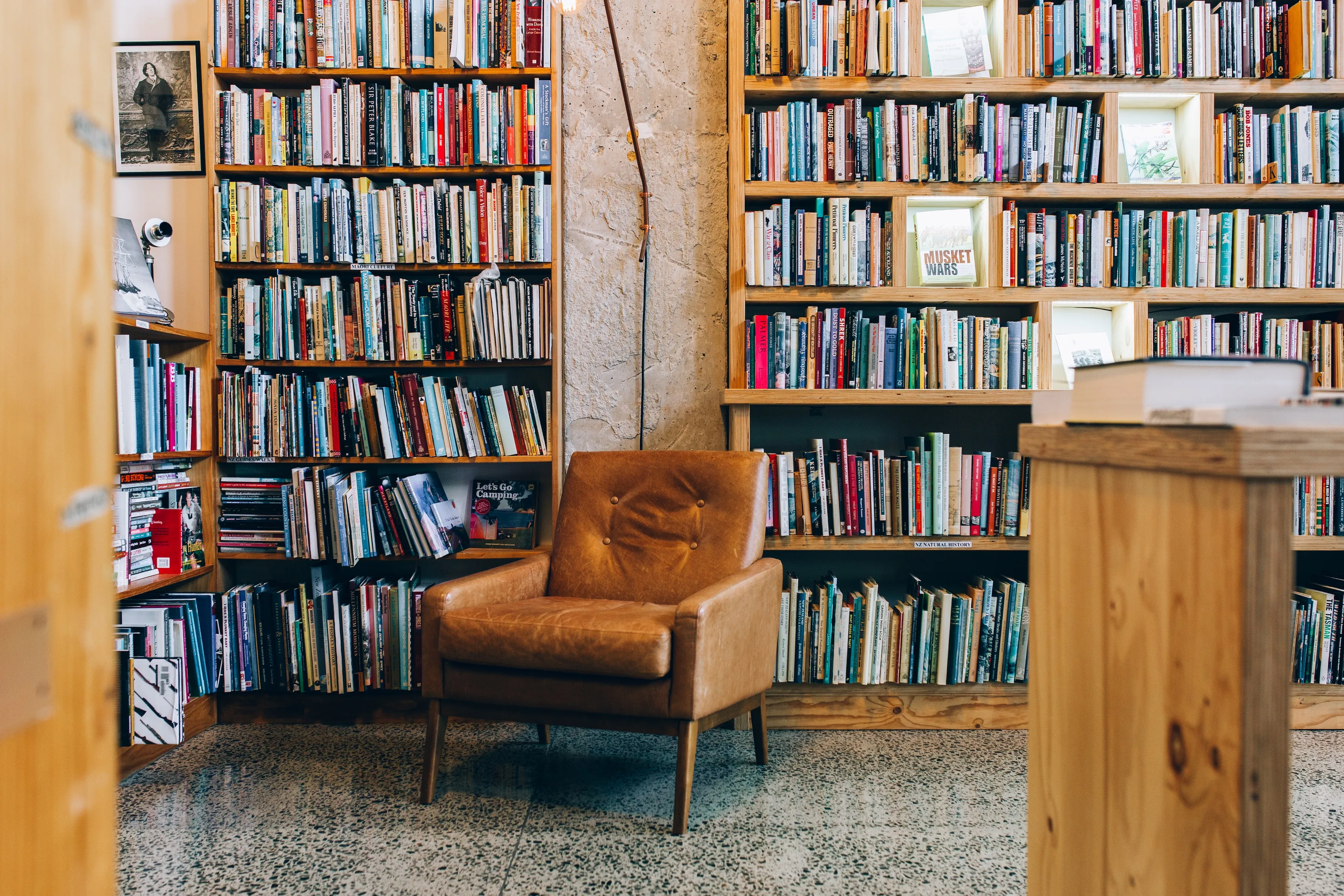 A cosy reading nook featuring a stylish brown leather chair surrounded by wooden bookshelves filled with a diverse collection of books.