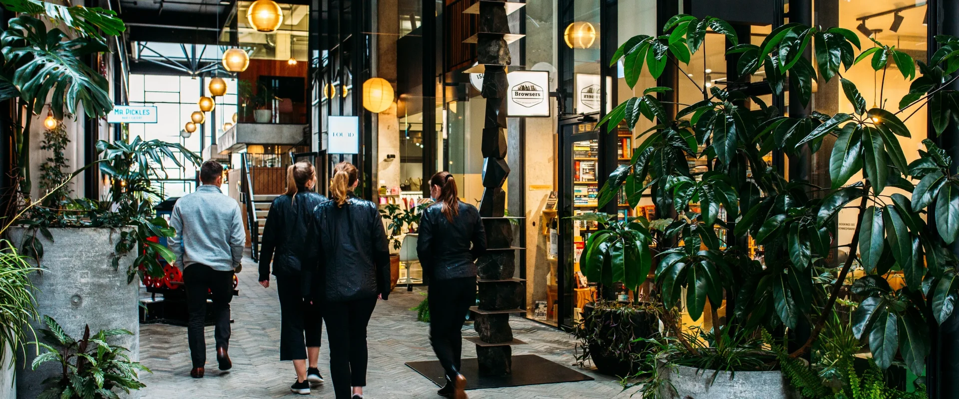 A vibrant indoor walkway in Hamilton featuring local shops, lush greenery, and decorative lighting.