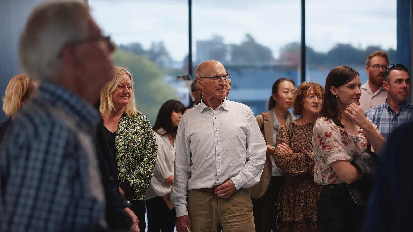 A diverse group of people engage in conversation at a local Hamilton community event. Expressions of interest and connection are evident, highlighting the vibrant spirit of support for local businesses and community experiences in the city.