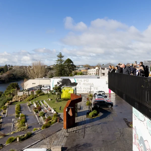 A panoramic view from a balcony in Hamilton, showcasing a vibrant community event. Attendees enjoy the riverside scenery, while nearby green spaces and colourful murals enhance the lively atmosphere of the city's cultural heart.
