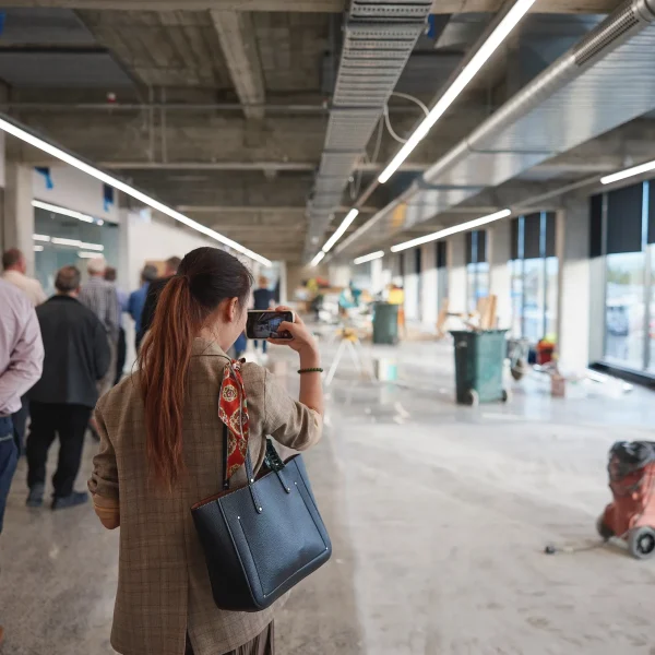 A woman captures an image in a newly renovated space, showcasing Hamilton's community development. The background features a group of people touring the local business site, highlighting support for the city's evolving heart.