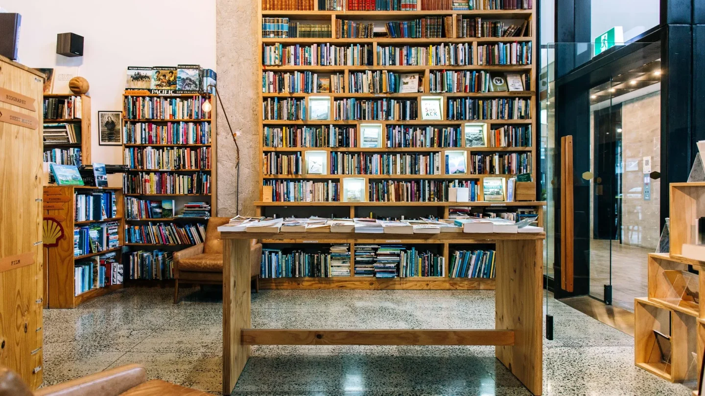 Cosy community library in Hamilton featuring extensive bookshelves filled with books, with a wooden table of books inviting local residents to explore.
